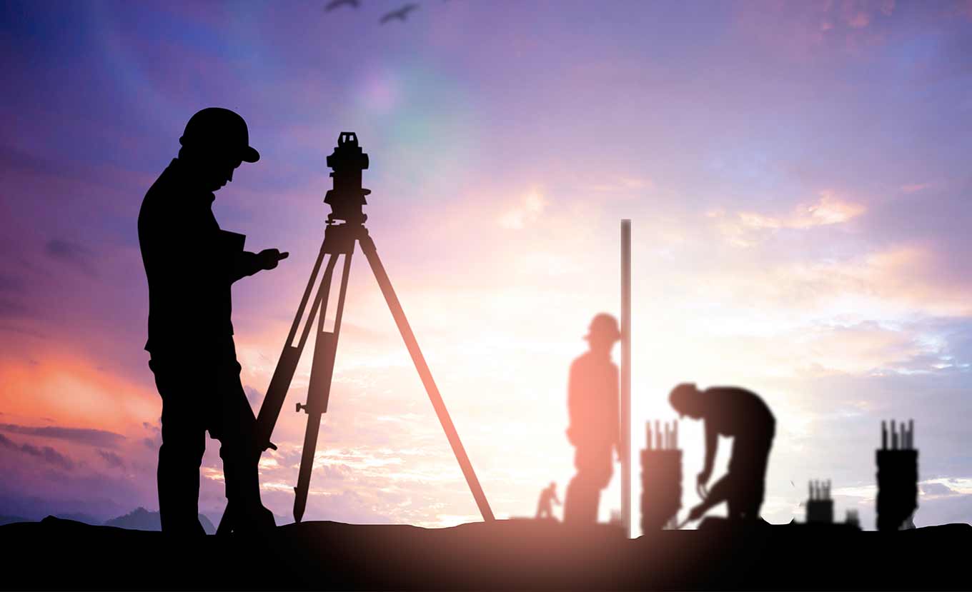 Surveyor using a tripod-mounted instrument at a construction site
